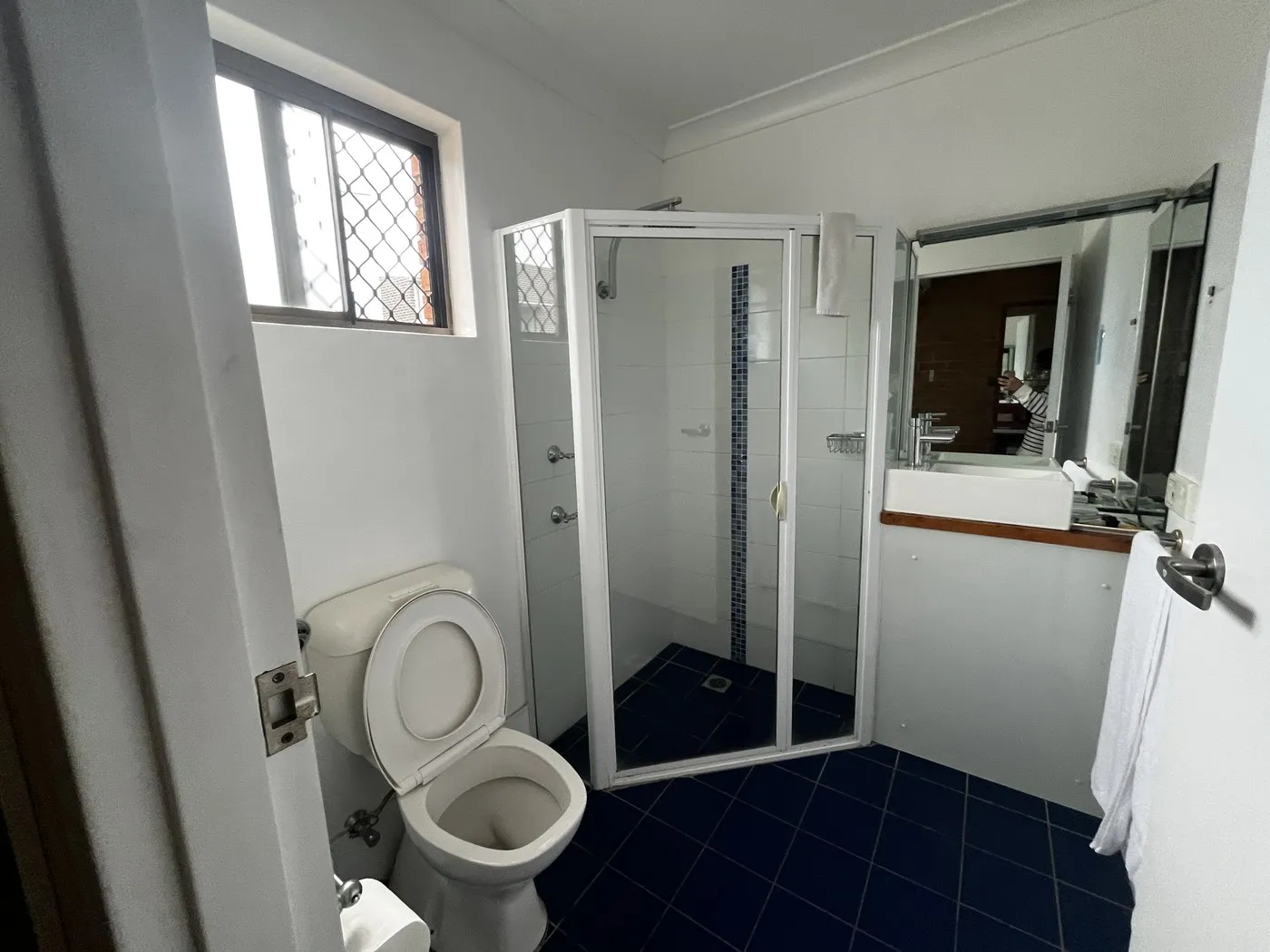 A bathroom with a glass shower screen, navy floor tiles and a vanity