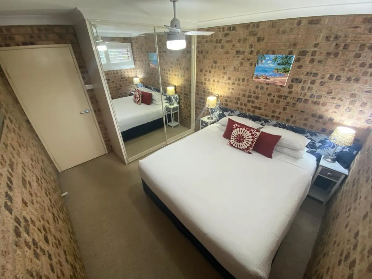A king bed with red and white cushions against a brick feature wall