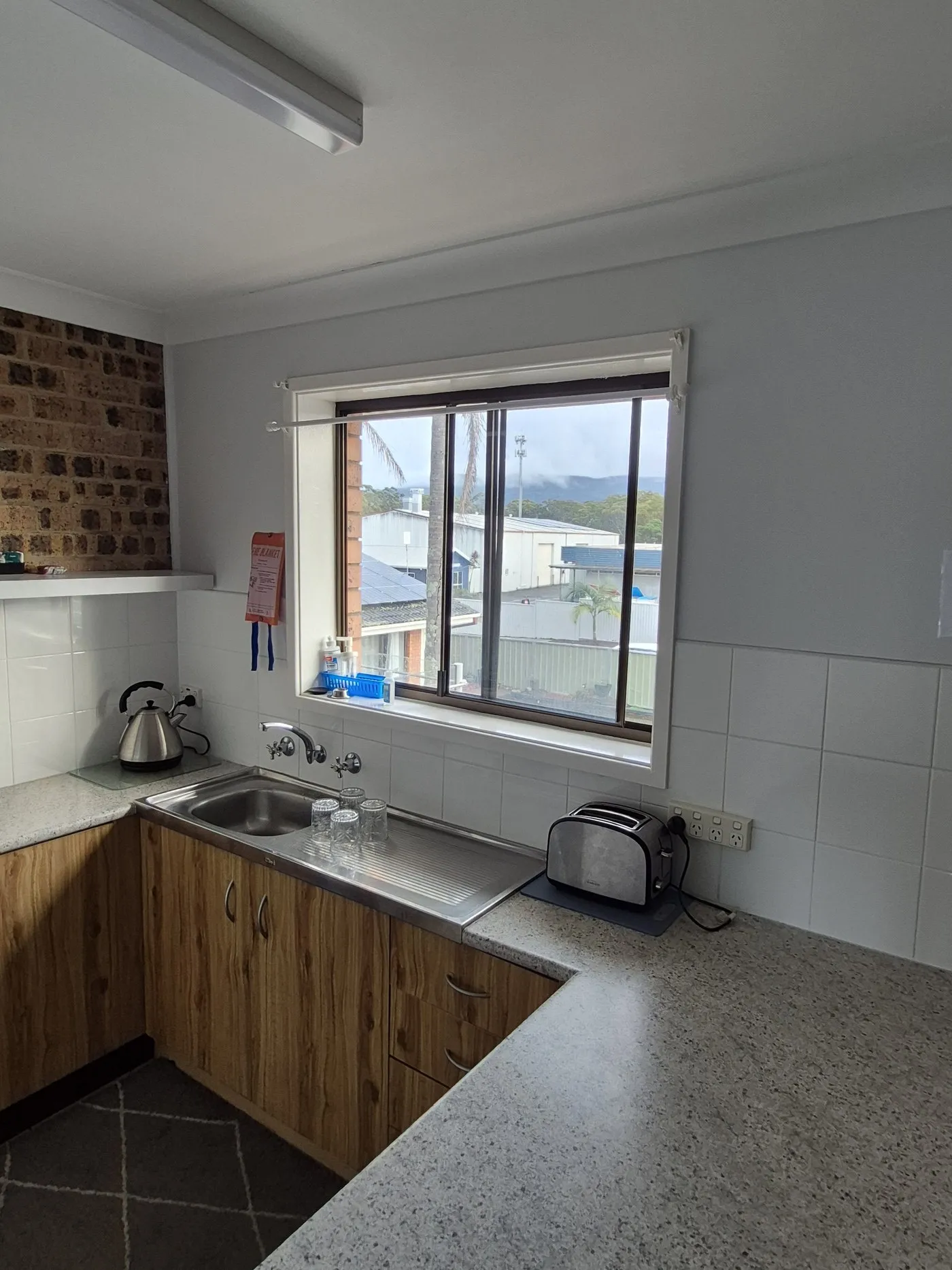 A kitchenette with timber cupboards, sink, toaster and kettle by a window