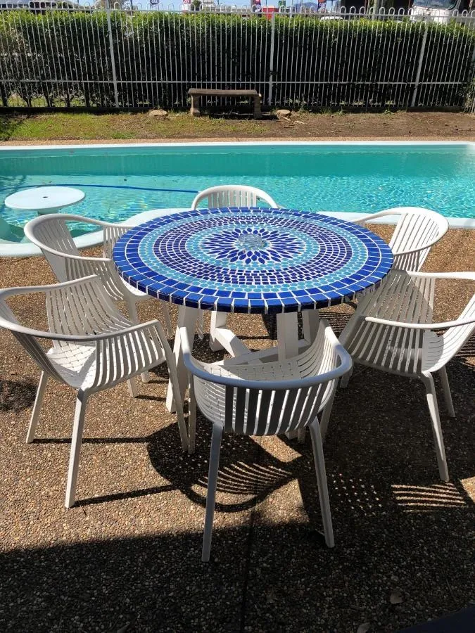 A blue and white mosaic table with white chairs beside the pool