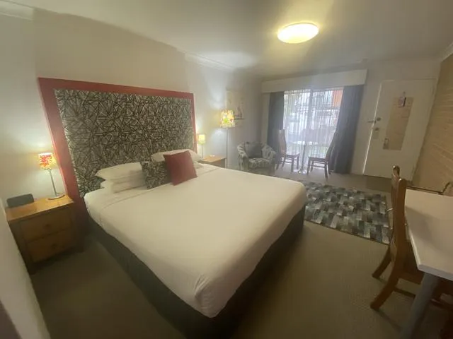 A Premier King room: king bed with a patterned bedhead, timber bedside table and desk chair