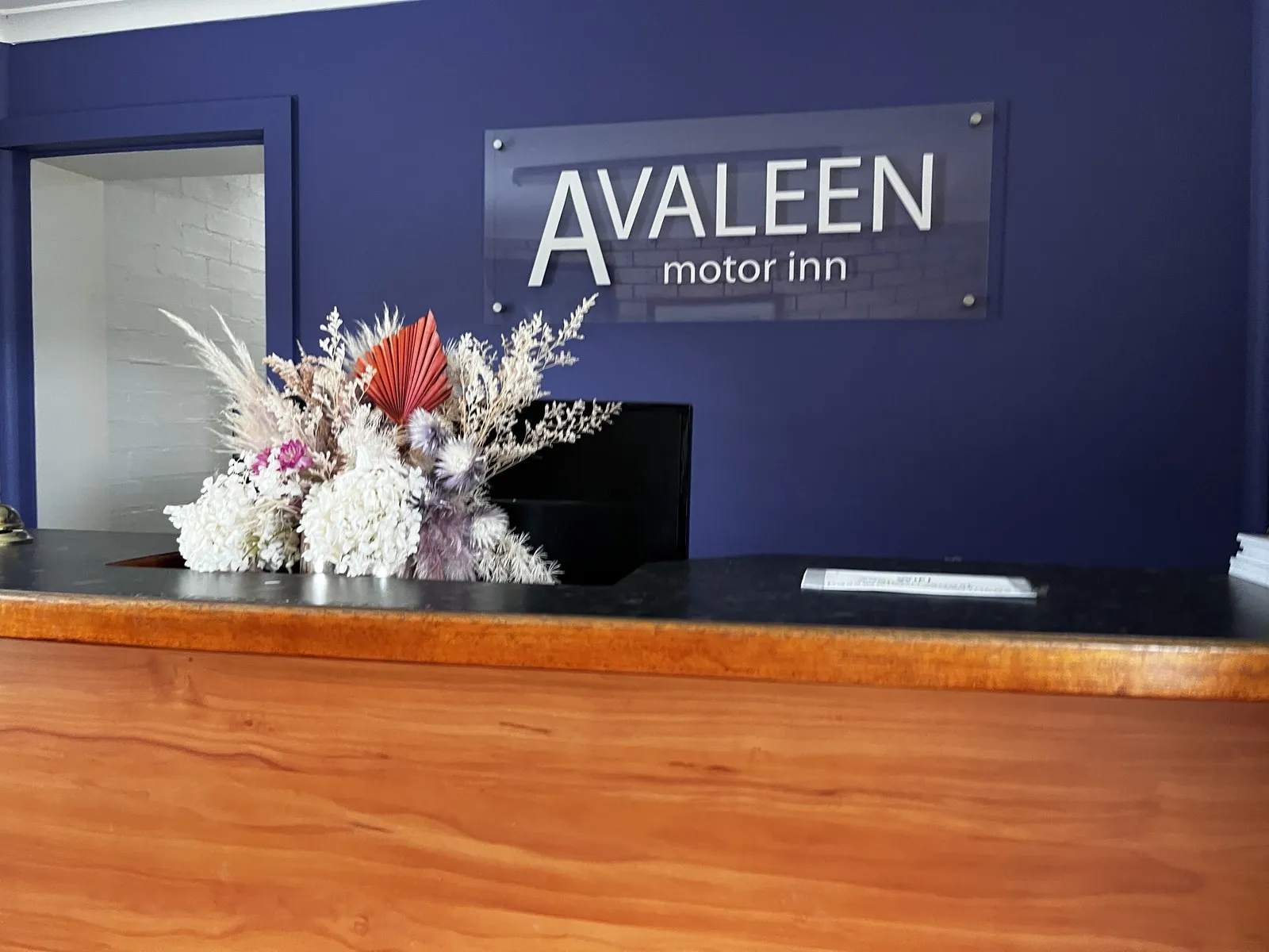 The Avaleen motor inn sign on the navy reception wall, with a dried flower arrangement on the timber counter