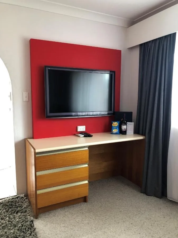 A desk with drawers and a wall-mounted TV on a red feature wall