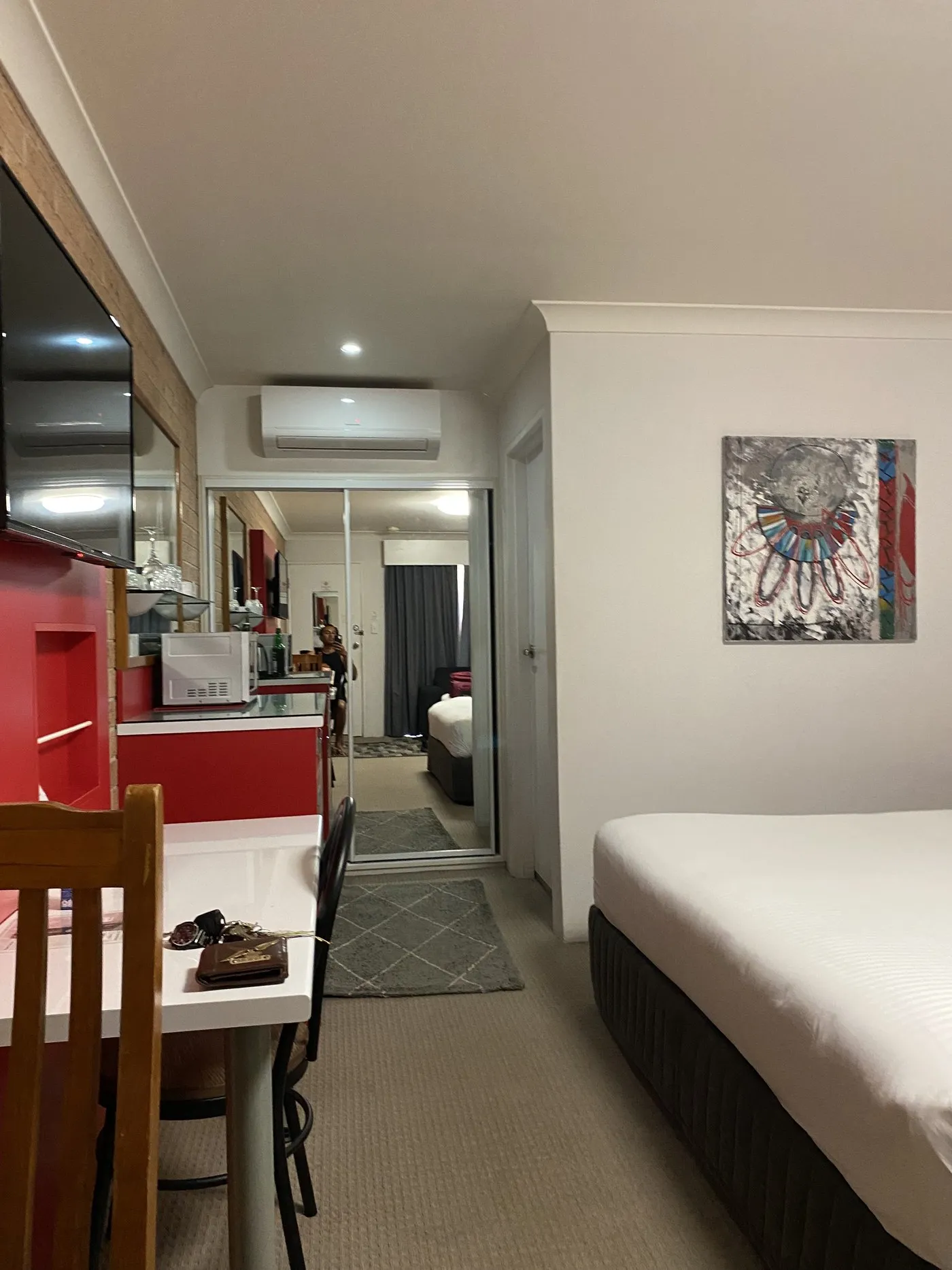 A room with a red kitchenette, dining table and bed