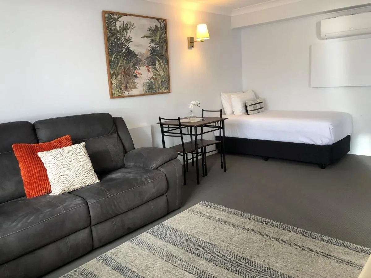 A room with a lounge, a small dining table and a made bed