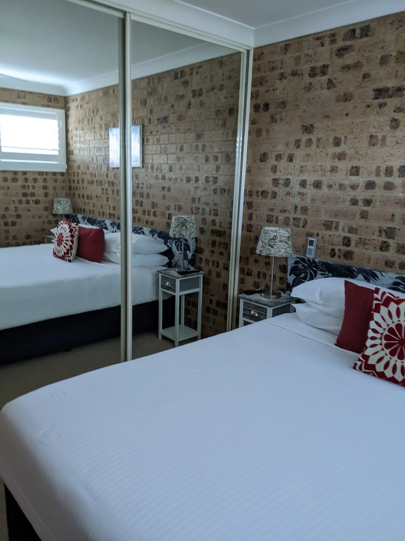 A room with a king bed, mirrored wardrobe and a feature brick wall