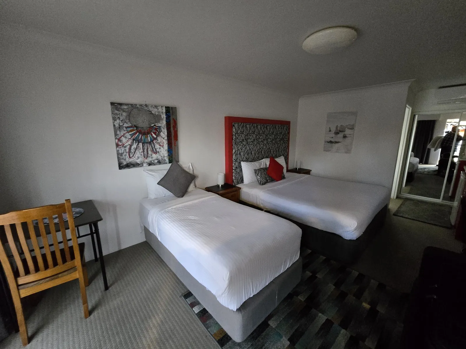 A twin room with a king bed and a single bed, a red upholstered bedhead and a timber desk and chair